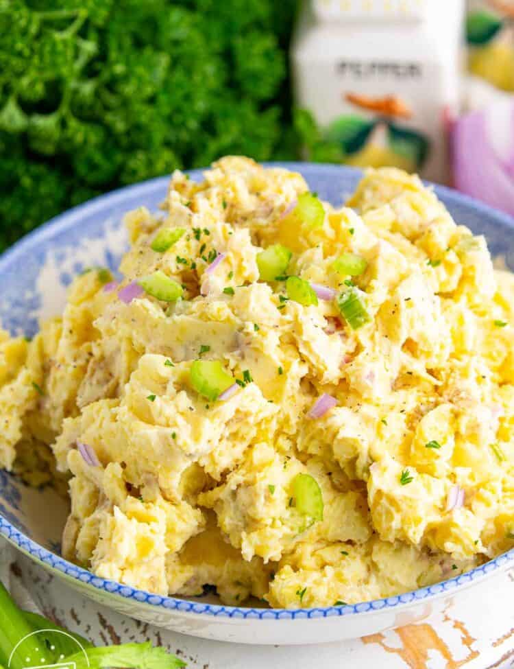 Close up of creamy smashed potato salad in a blue serving bowl, made with tender gold potatoes, mayonnaise dressing, celery, and red onion, with fresh parsley sprinkled on top.