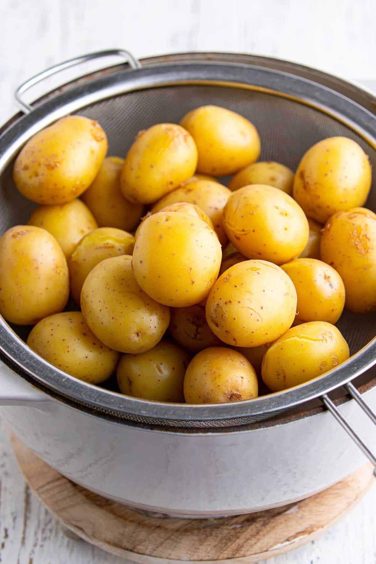 Cooked baby gold potatoes draining in a fine mesh strainer after boiling for creamy smashed potato salad.