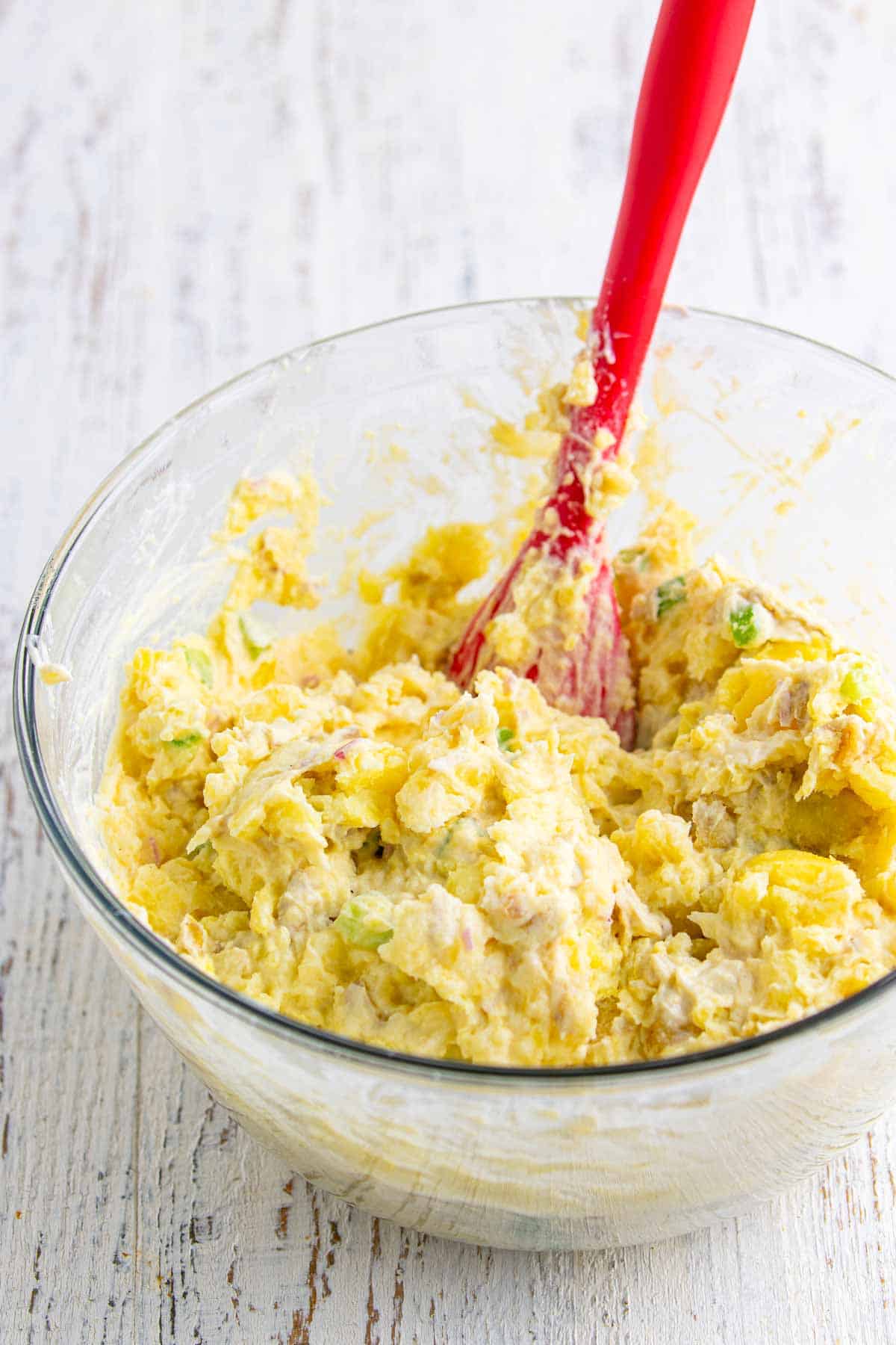 Smashed potatoes mixed with the creamy dressing in a glass bowl for creamy smashed potato salad.