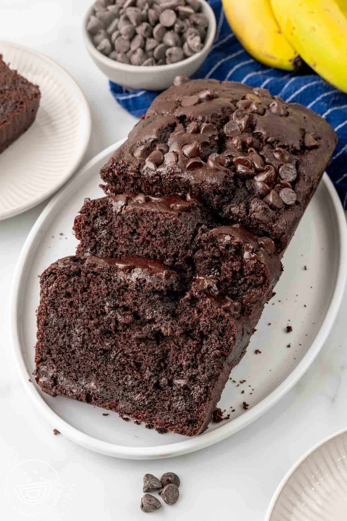 an oval platter holding a loaf of chocolate banana bread that has been sliced. The slices show lots of extra chocolate chips inside.