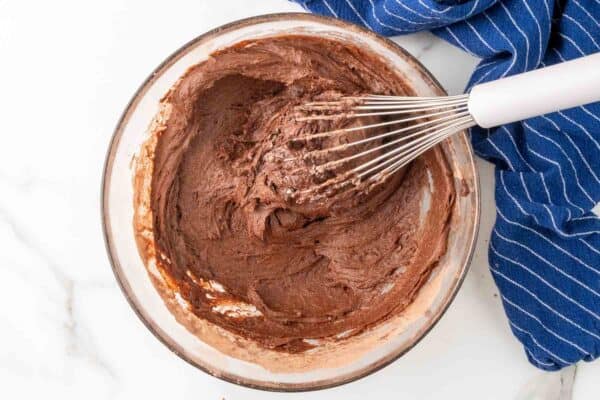 banana bread batter whisked in a glass mixing bowl next to a blue and white striped towel.