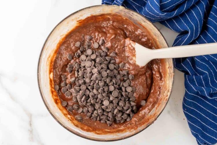 Chocolate chips added to chocolate banana bread batter with a spatula.