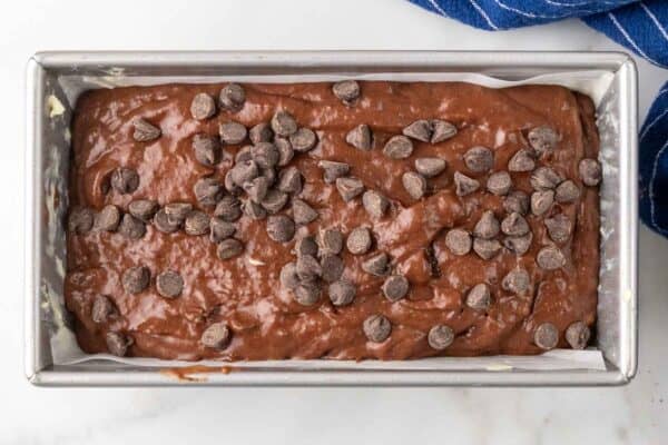 chocolate banana bread batter in a parchment lined loaf pan, topped with extra chocolate chips.