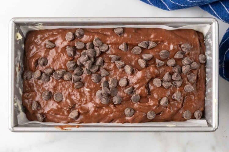 chocolate banana bread batter in a parchment lined loaf pan, topped with extra chocolate chips.
