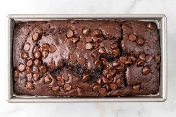 baked double chocolate banana bread topped with melted chocolate chips, in a rectangular metal loaf pan.