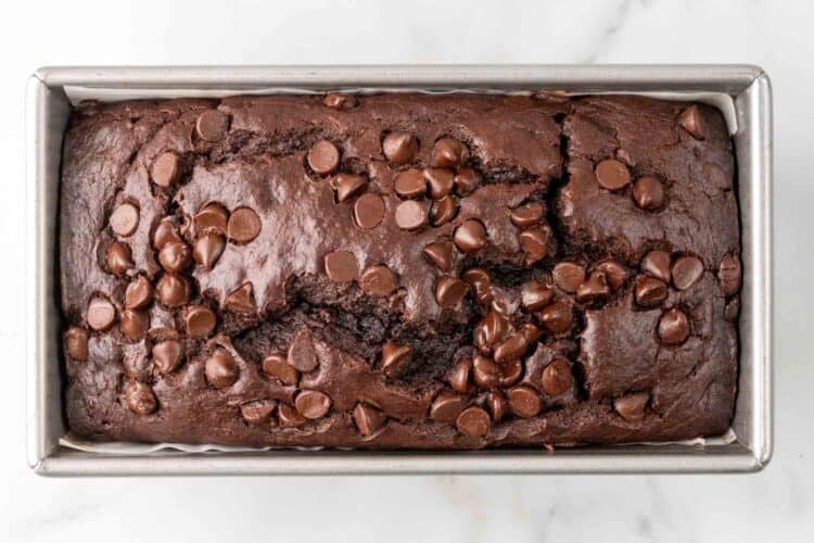 baked double chocolate banana bread topped with melted chocolate chips, in a rectangular metal loaf pan.