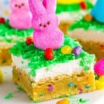 Easter sugar cookie bar topped with coconut frosting, green dyed coconut, a pink Peeps bunny, and colorful jelly beans on a soft sprinkle filled sugar cookie base.