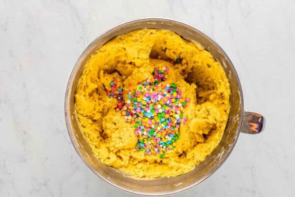 Cookie dough in a mixing bowl topped with colorful confetti sprinkles.