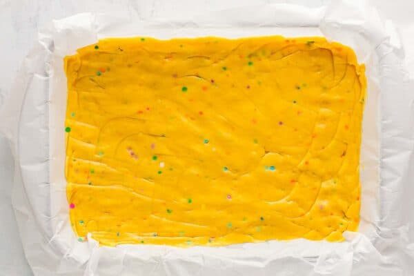 Sugar cookie dough spread evenly in a parchment lined baking dish before baking.