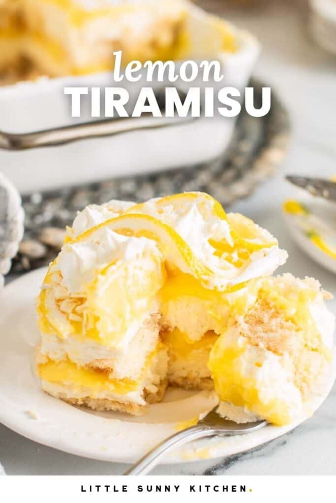 A slice of lemon tiramisu with layers of ladyfingers, lemon curd, and whipped mascarpone topped with cream and lemon slices on a white plate.