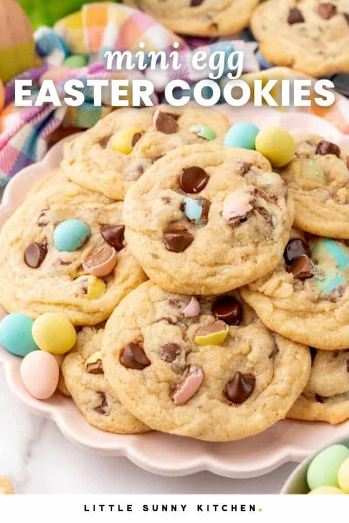 a pink scalloped platter of chocolate chip cookies with cadbury mini eggs inside. Text overlay says "mini egg Easter cookies"