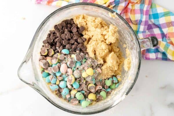 chocolate chips and crushed cadbury mini eggs added to cookie dough in a large mixer bowl.