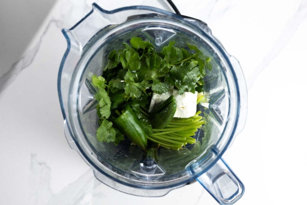ingredients for Peruvian green sauce (aji verde) in a blender with cilantro, jalapeños, garlic, and cheese
