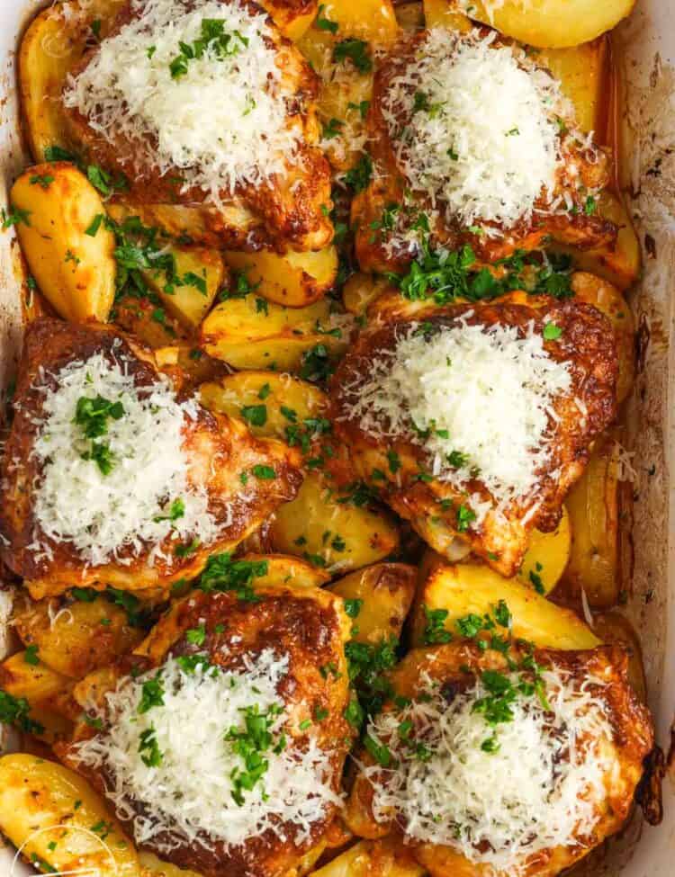 overhead view of a 9x13 baking dish of cooked potato wedges topped with bone in chicken thighs. each piece of chicken is topped with grated parmesan cheese.