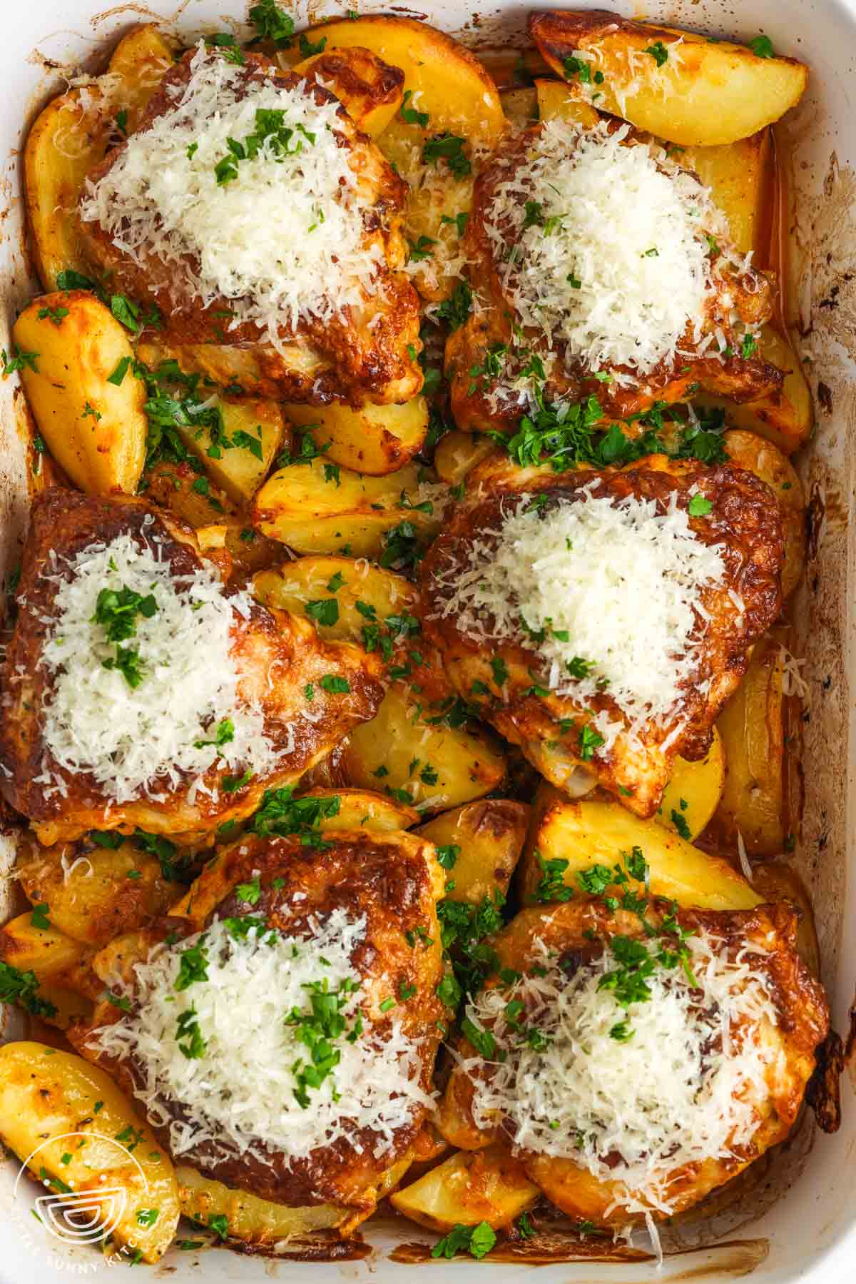 overhead view of a 9x13 baking dish of cooked potato wedges topped with bone in chicken thighs. each piece of chicken is topped with grated parmesan cheese.