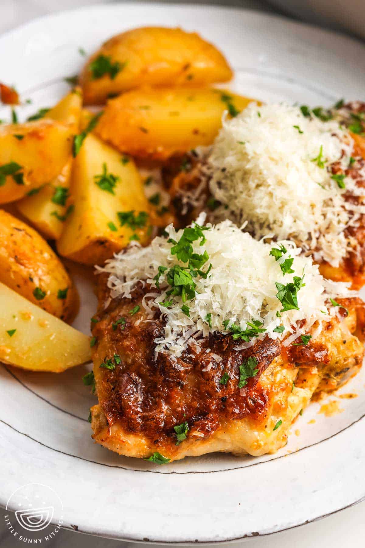 a plate with two baked chicken thighs and a side of roasted potatoes.