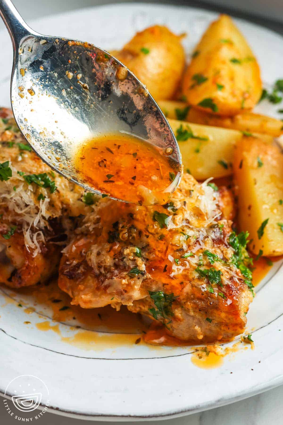 a plate of chicken thighs and potatoes. A spoon is adding pan sauce to the chicken.