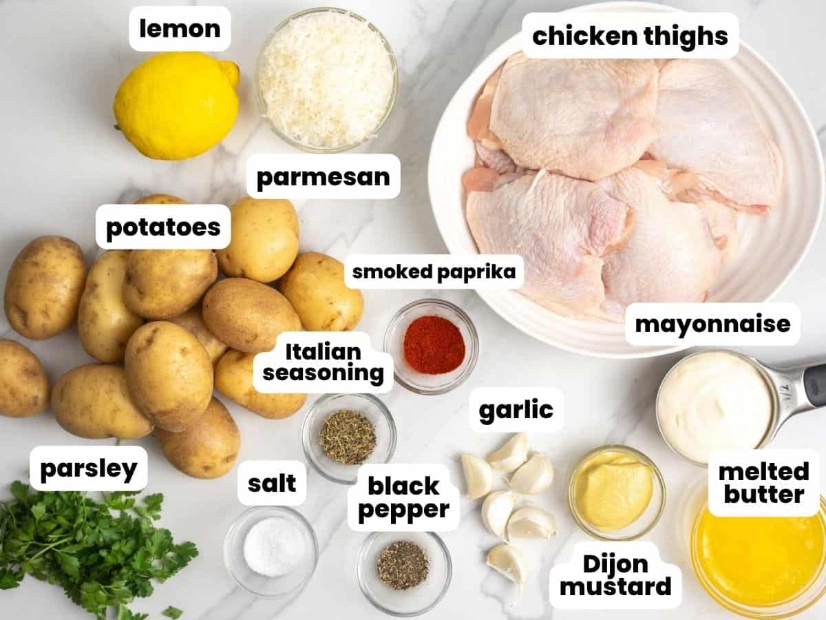 a plate of raw bone-in chicken thighs next to a pile of potatoes, dijon mustard, and other ingredients to make baked chicken thighs.