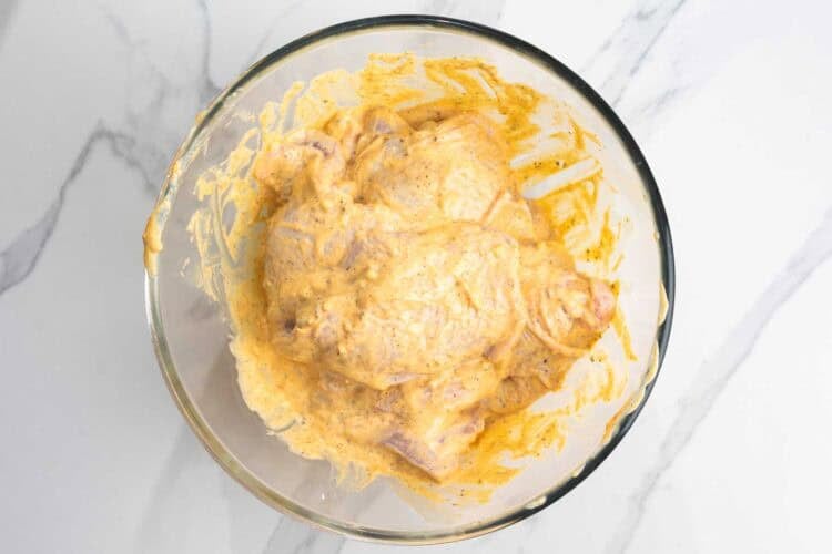 raw chicken thighs covered in mayo and mustard mixture in a glass mixing bowl.