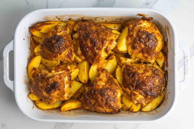 baked chicken thigs with potatoes in a rectangular baking dish. The six thighs on on top of the potatoes, and everything is well browned.