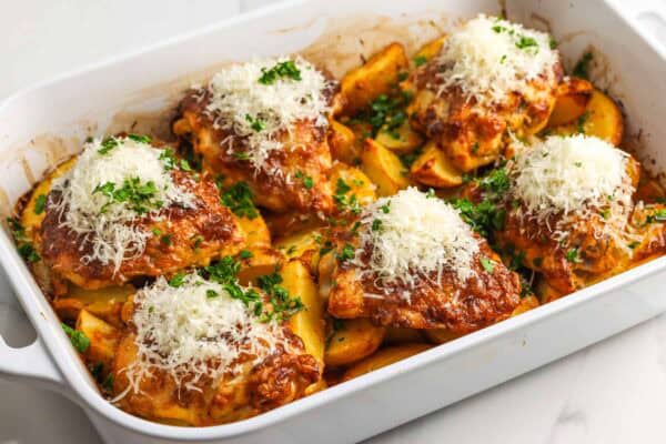 Chicken thighs and potatoes in a baking dish, finished with grated parmesan cheese and chopped parsley.