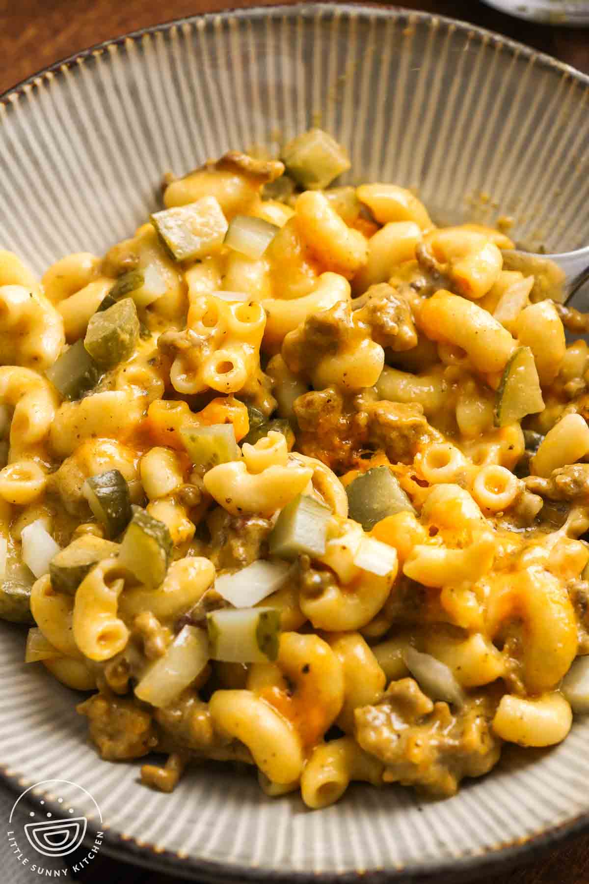 a ceramic bowl holding a serving of cheeseburger mac and cheese topped with chopped dill pickles.