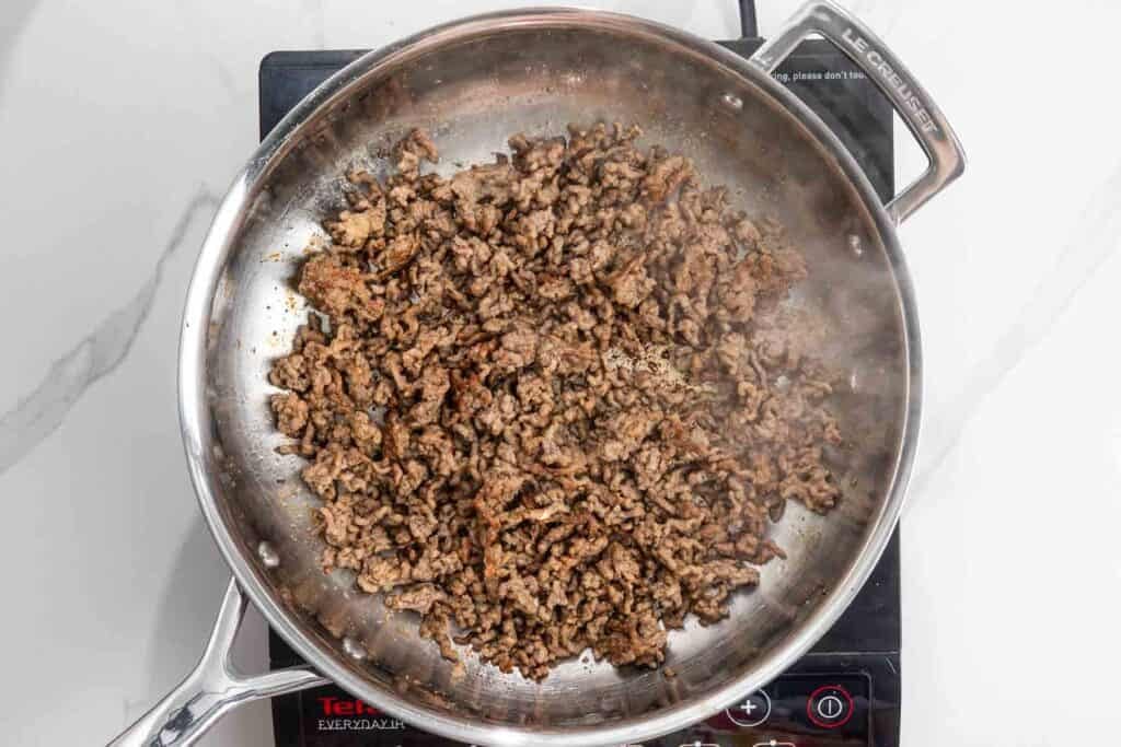 Ground beef cooking in a stainless steel skillet set over an electric burner.