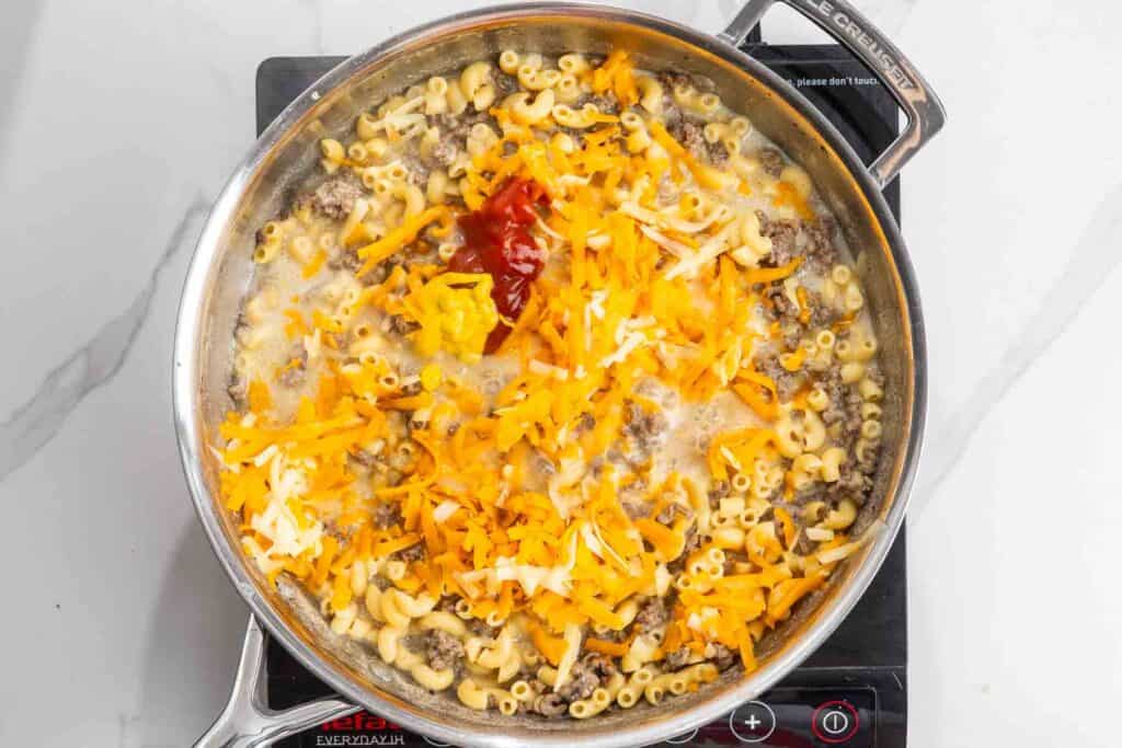 grated cheese, ketchup, and mustard added to macaroni and beef to create cheeseburger mac and cheese.