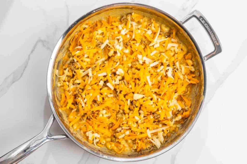 Extra cheese added to cheeseburger mac in a stainless steel skillet.