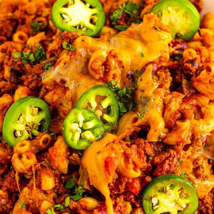 Bowl of chili macaroni with ground beef, beans, melted cheese, sliced jalapeños, and chopped cilantro