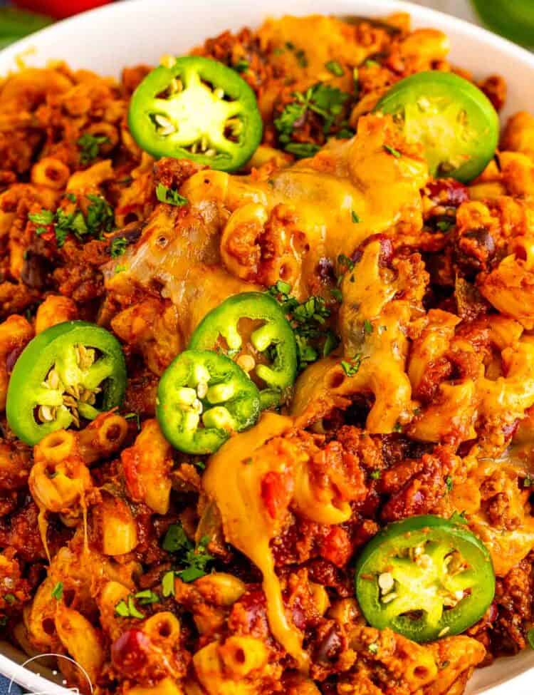 Bowl of chili macaroni with ground beef, beans, melted cheese, sliced jalapeños, and chopped cilantro