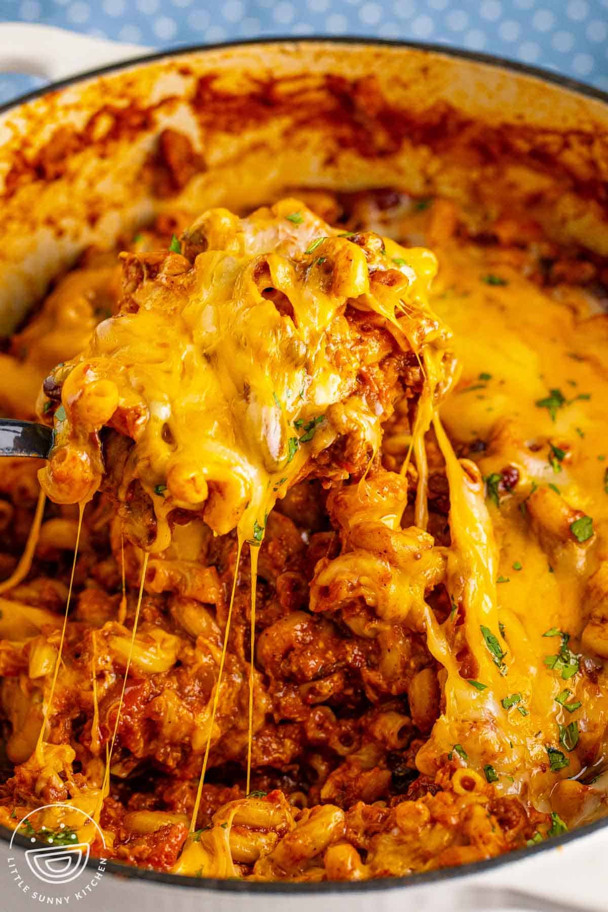 Spoonful of chili macaroni with elbow pasta, beef chili, beans, and melted cheese pulled from a Dutch oven.
