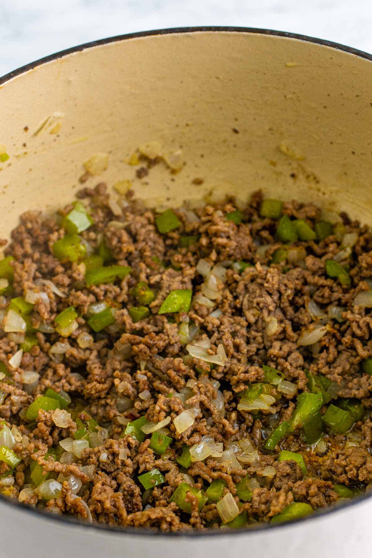 Ground beef cooked with diced onion and green bell pepper in a Dutch oven.