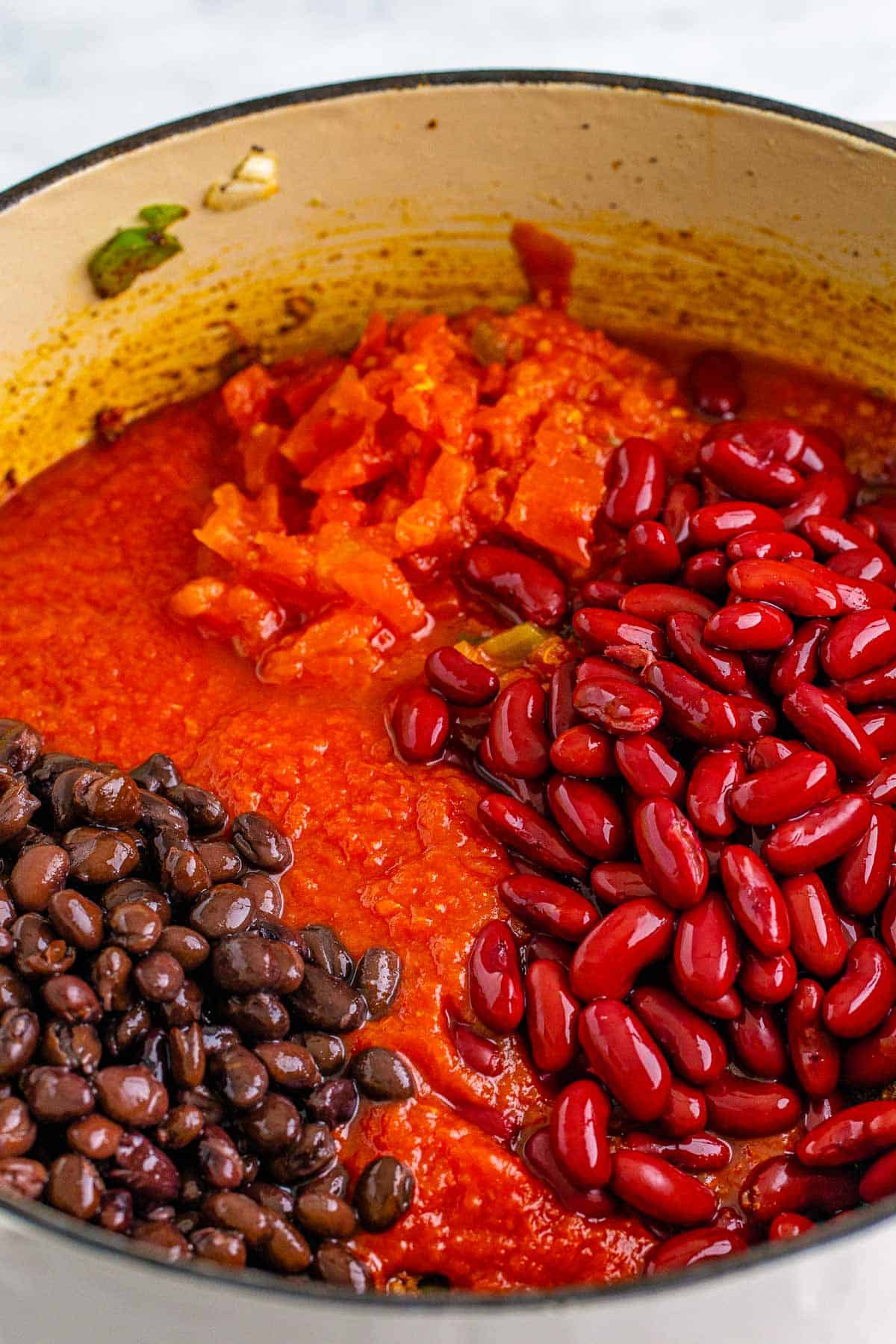 Tomatoes, black beans, and kidney beans added to a pot for chili macaroni.