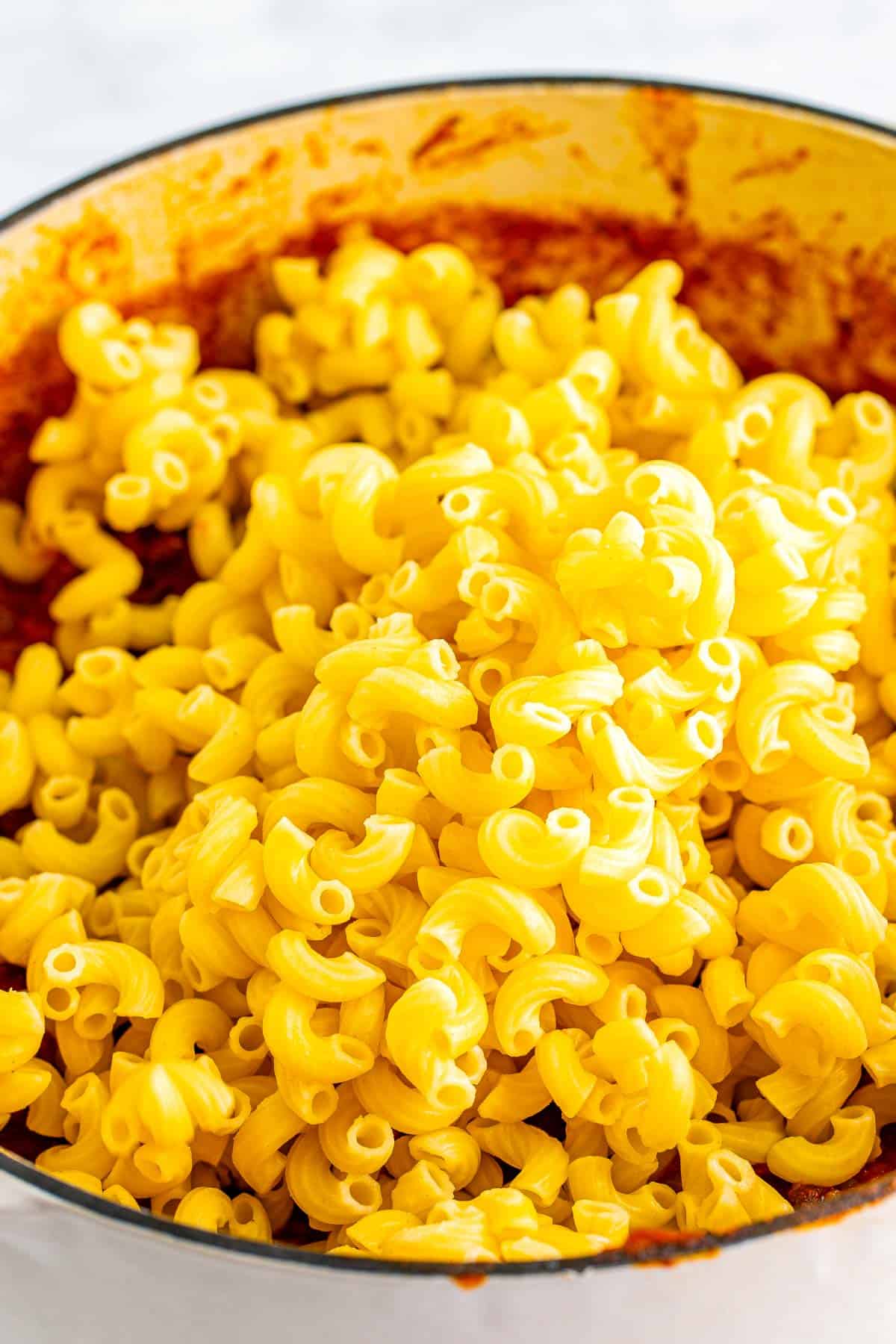 Cooked elbow macaroni added to the chili mixture in a Dutch oven.