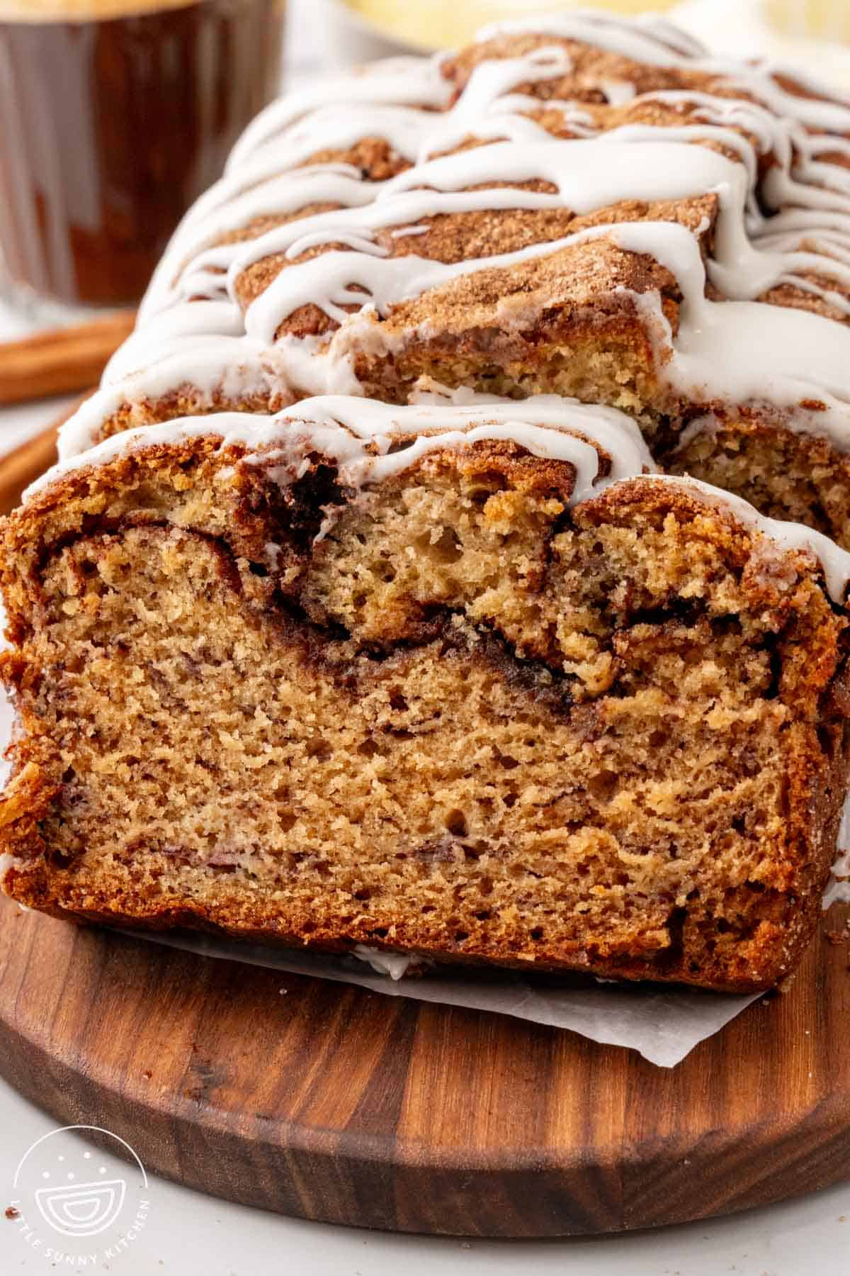 a loaf of cinnamon swirl banana bread, sliced and siet on a wooden board.