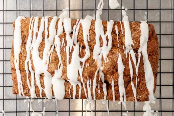 a loaf of cinnamon banana bread on a wire rack. white icing is drizzled over the top.