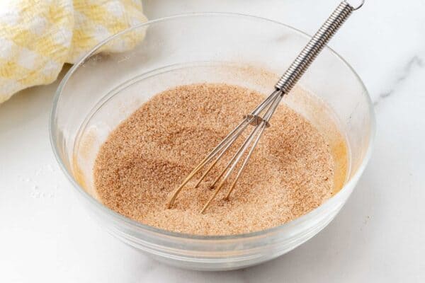 cinnamon and sugar mixed in a small glass bowl with a small wire whisk.