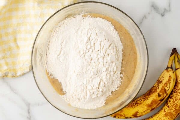dry ingredients added to wet ingredients to make banana bread batter in a large glass mixing bowl.