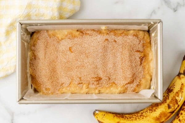 cinnamon sugar spread over banana bread batter in a parchment lined loaf pan.
