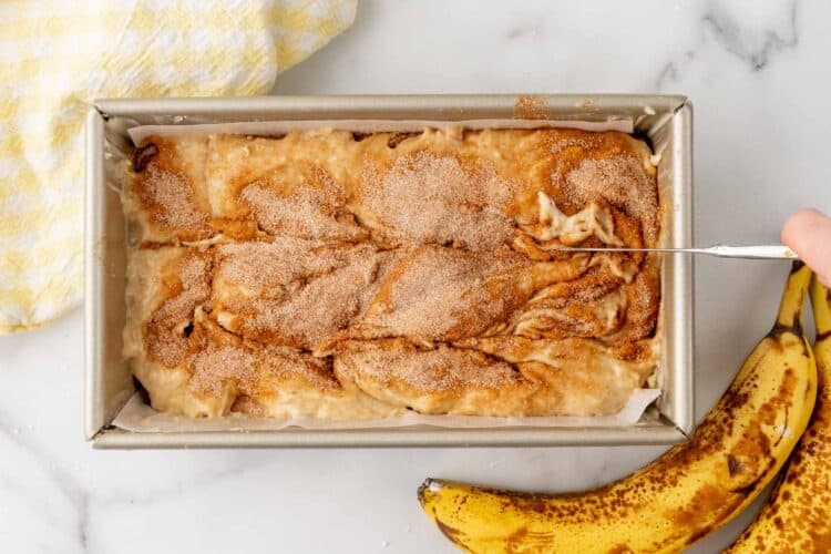 using a knife to create swirls in cinnamon sugar banana bread batter.