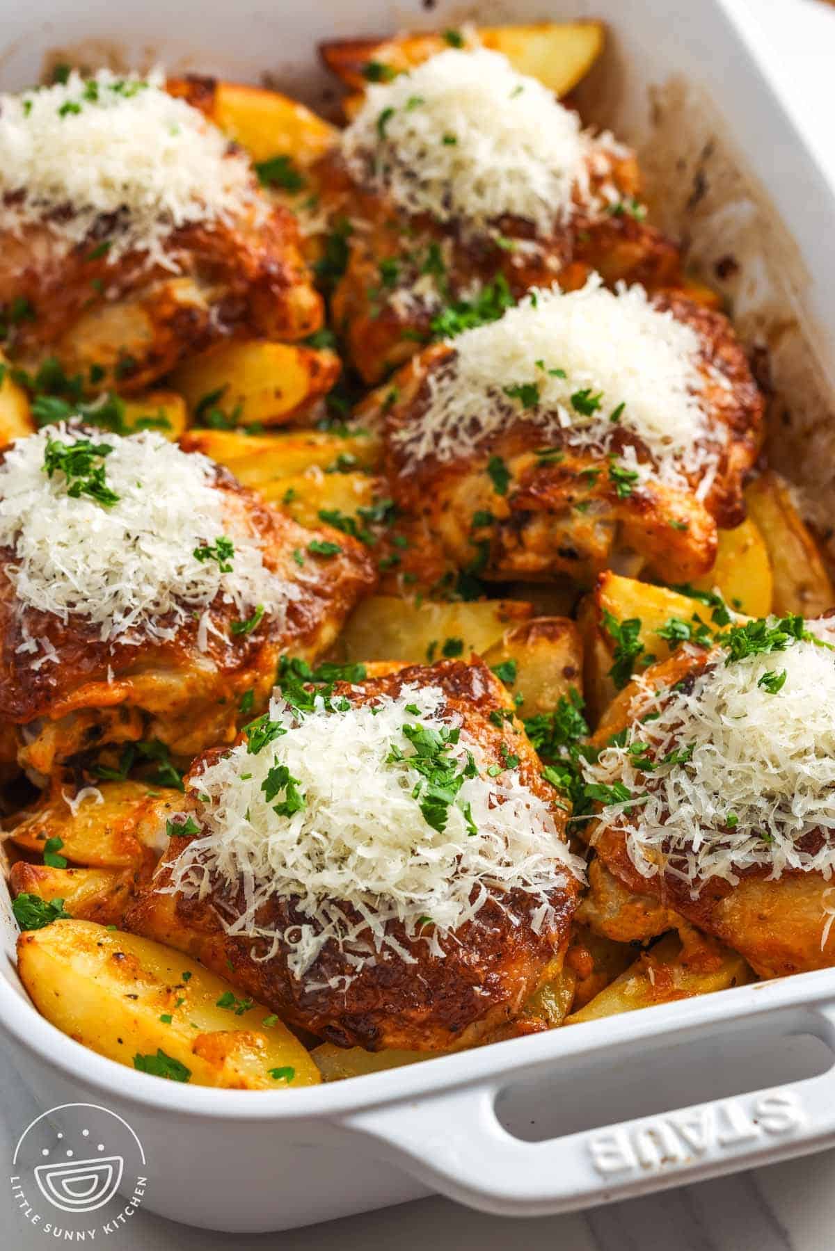 Chicken thighs and potatoes in a baking dish, finished with grated parmesan cheese and chopped parsley.