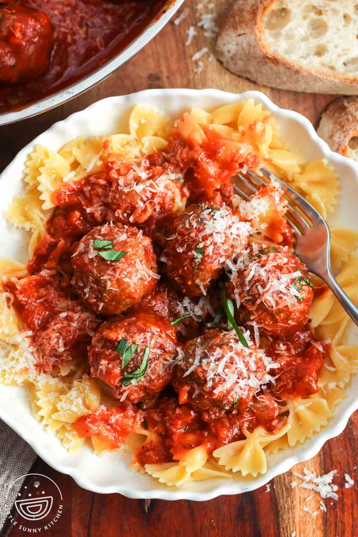 a plate of bowtie pasta topped with ricotta meatballs in tomato sauce. Next to the bowl is sliced italian bread.