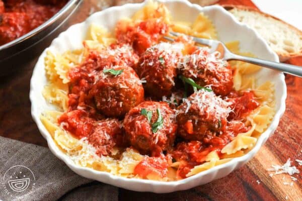 a bowl of meatballs and sauce served over farfalle pasta.