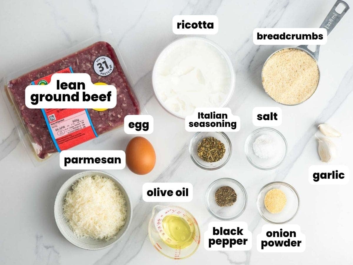 Ingredients for ricotta meatballs, including ground beef, breadcrumbs, ricotta cheese, egg, and seasonings, all measured and arranged on a marble counter.