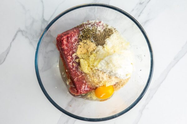Ground beef in a glass bowl with seasonings, egg, and ricotta cheese.