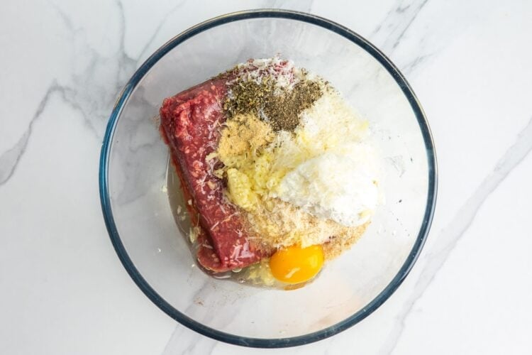 Ground beef in a glass bowl with seasonings, egg, and ricotta cheese.
