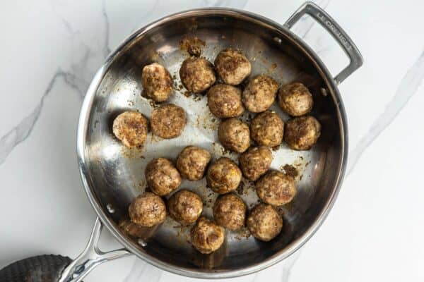 21 cooked ricotta meatballs in a stainless steel skillet.
