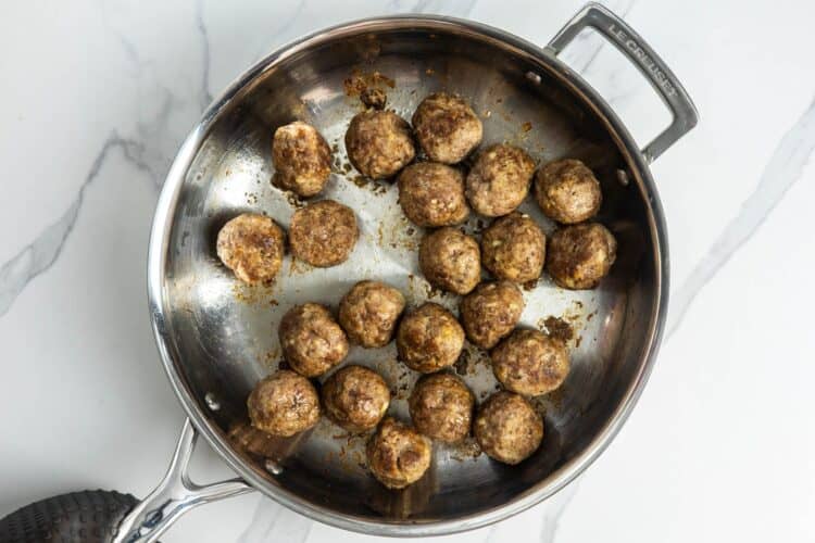 21 cooked ricotta meatballs in a stainless steel skillet.
