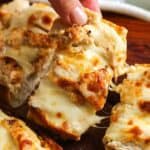 Hand picking up a cheesy slice of chicken Alfredo garlic bread with melted mozzarella and golden ciabatta.